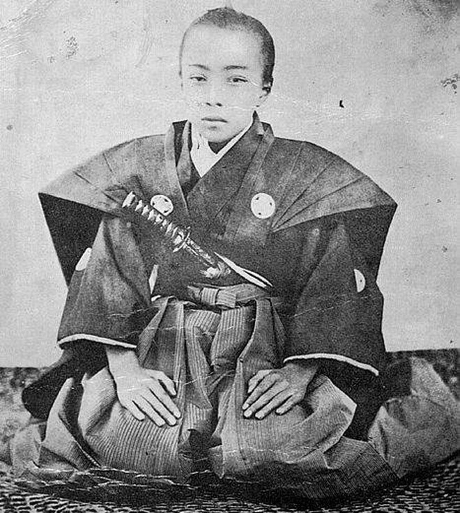 Kneeling young man in traditional Japanese samurai kimono with sword tucked in his sash